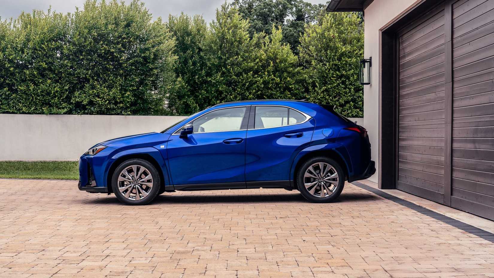 Foto estática do perfil lateral de um Lexus UX Hybrid F-SPORT 2026 azul estacionado em uma garagem.