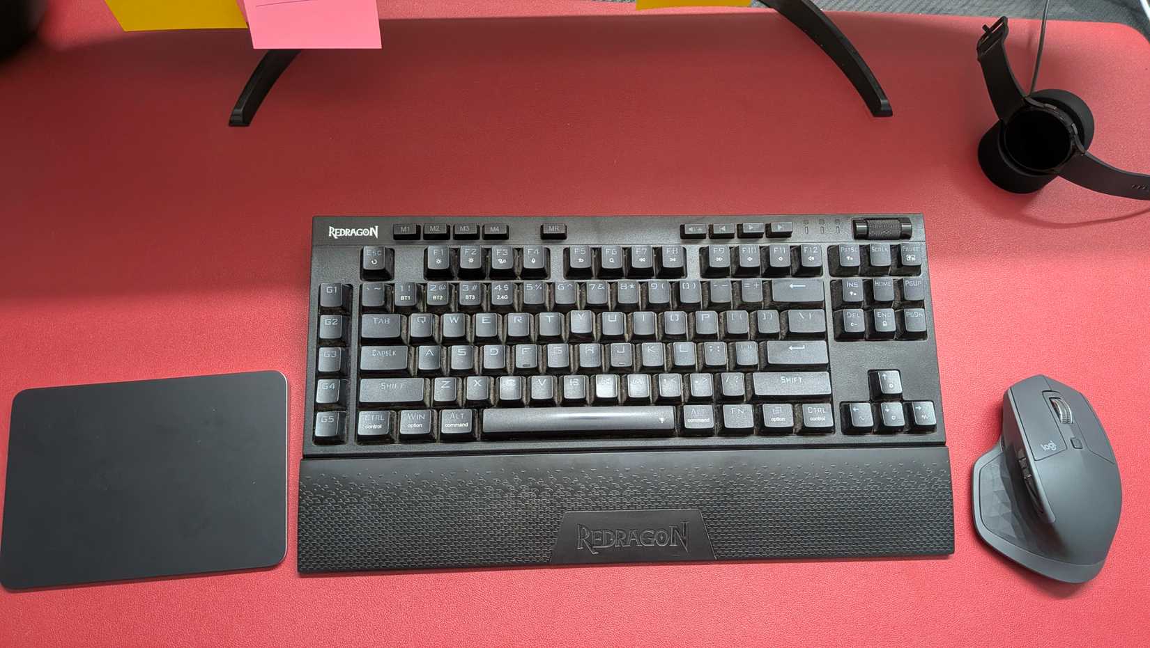 A red deskmat with a mouse, keyboard, and Apple Magic trackpad.
