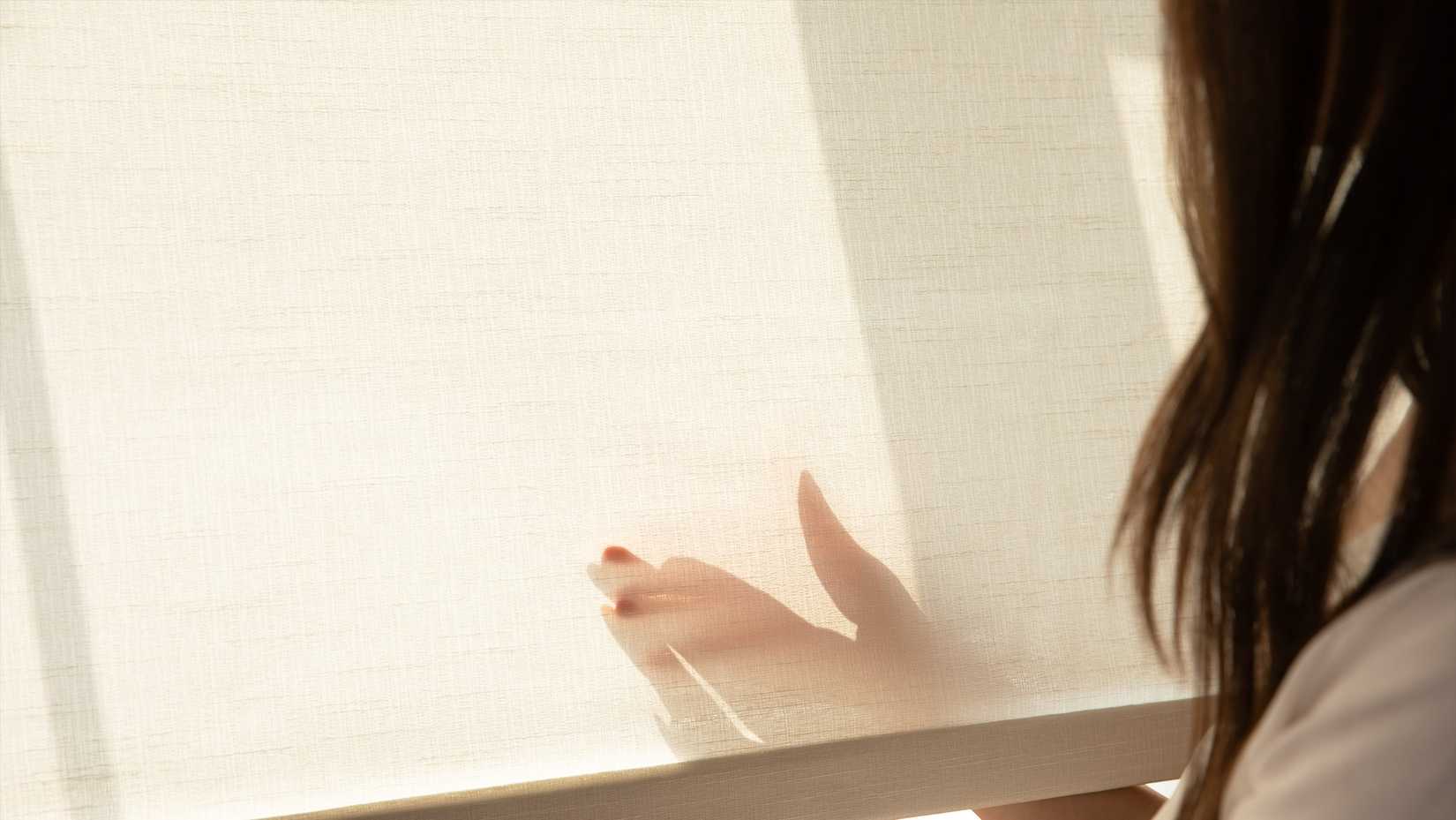 woman holding an allesin motorized sunshade at an angle to show the material construction