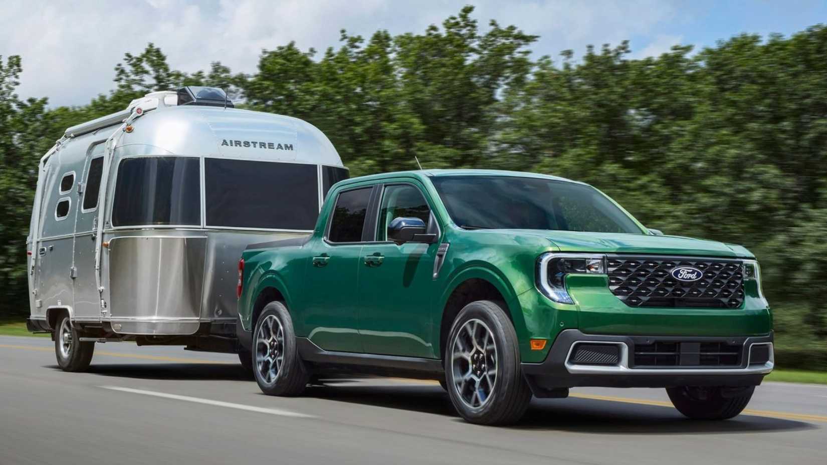 Dynamic front 3/4 shot of a green 2025 Ford Maverick towing a trailer on a country road.