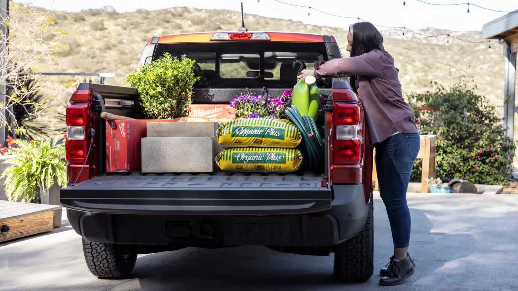 Shot of a woman loading gardening equipment in the bed of a red Ford Maverick.