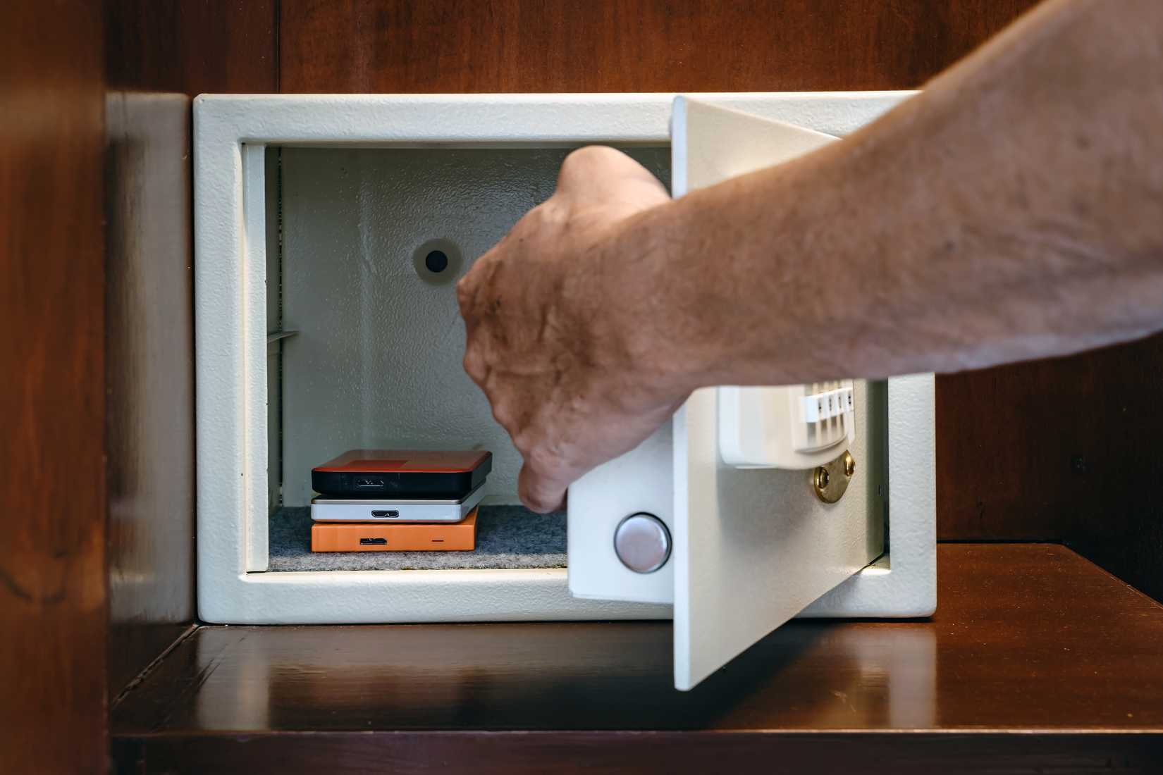 Uma imagem da mão de um homem colocando um disco rígido externo em um cofre para proteger seus dados