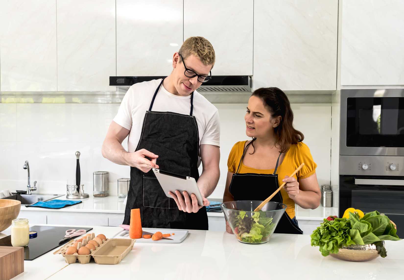 Couple cooking in kitchen and looking at ipad for salad recipes.