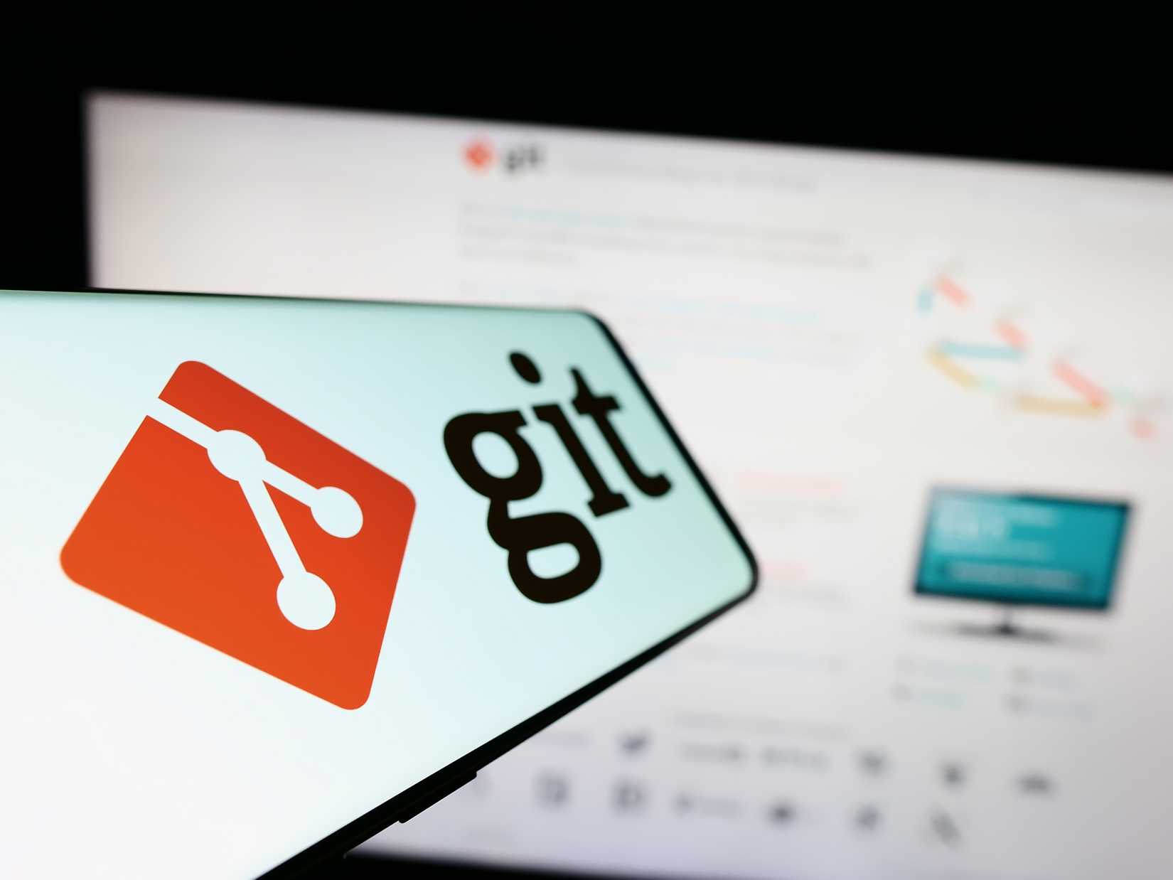 A mobile phone with logo of distributed version control system Git on screen in front of website. 