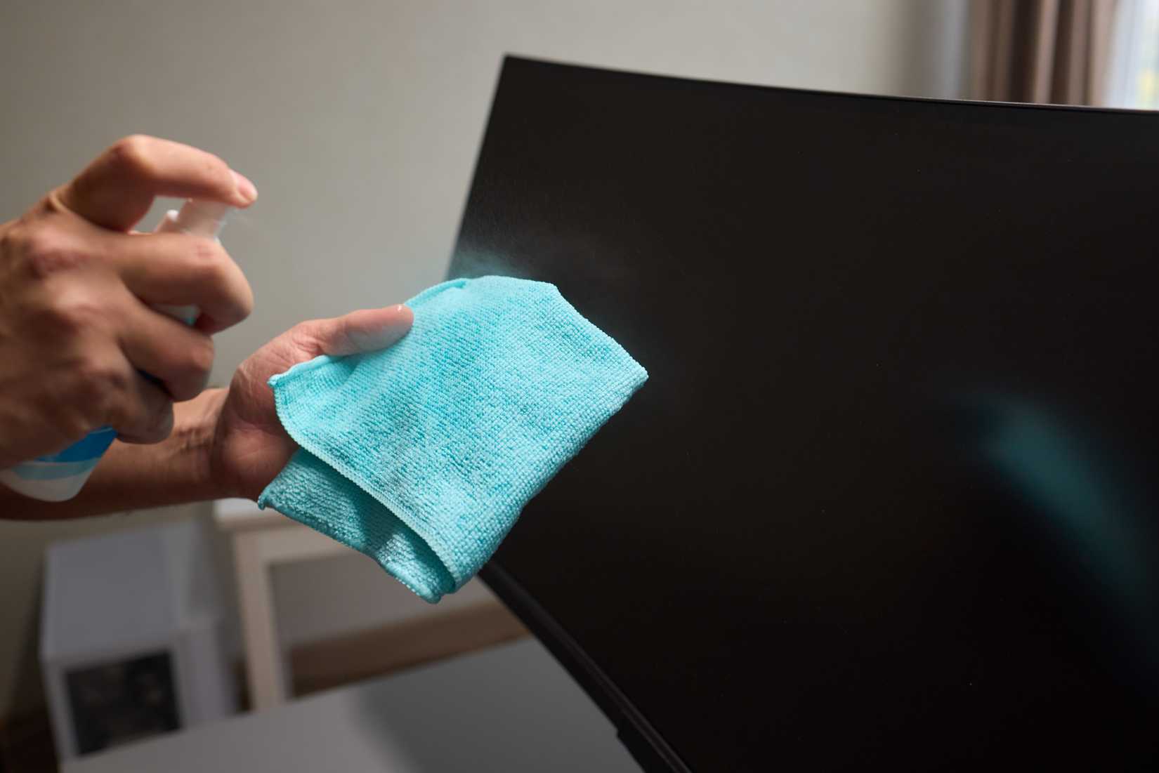 Someone uses a spray bottle to clean a TV screen.