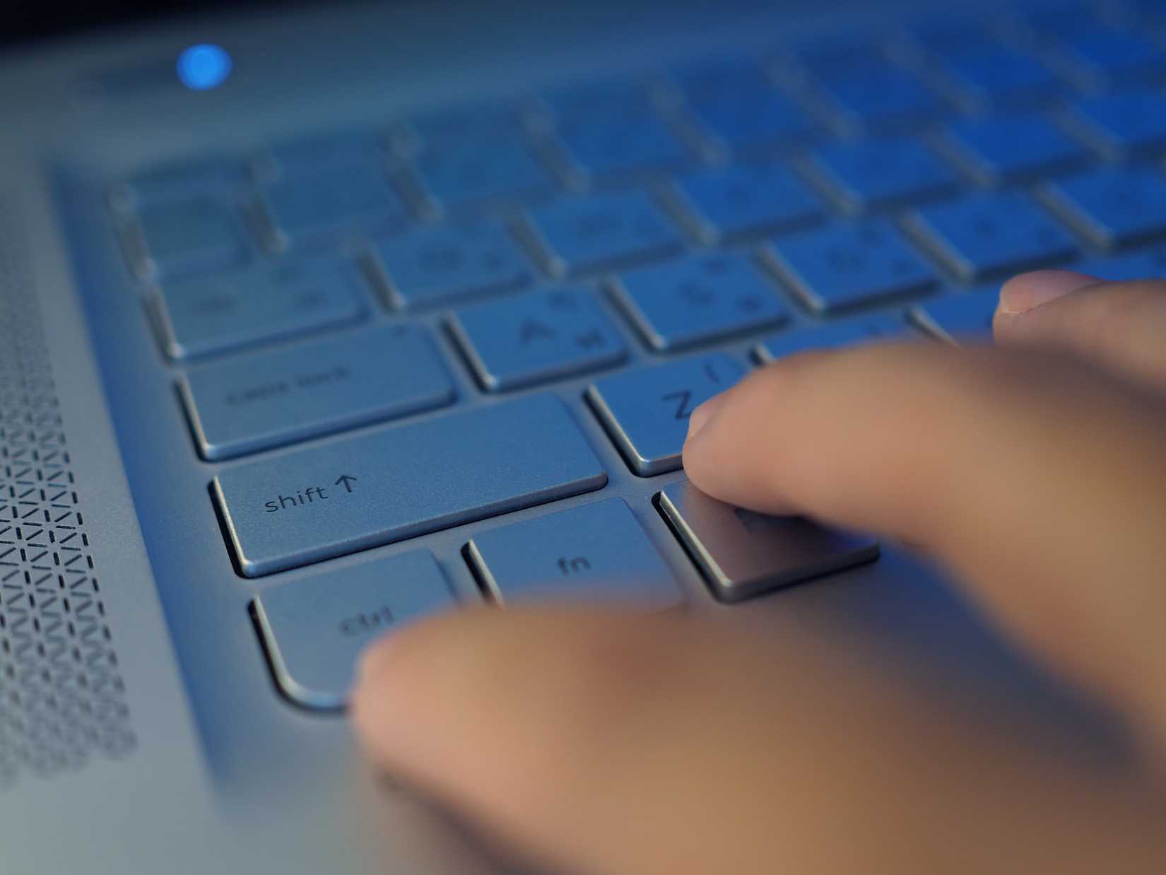 Close-up perspective on a silver aluminum laptop keyboard, fingers pressing a shortcut "Ctrl + Z."