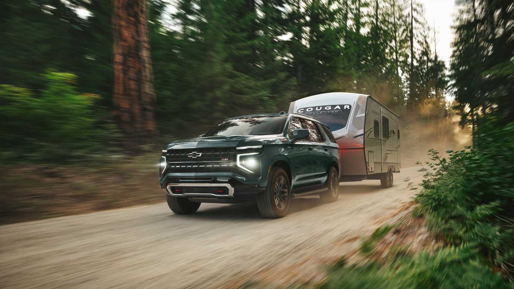 Toma dinámica de 3/4 del frente de una Chevrolet Tahoe 2025 arrastrando un remolque por un camino de tierra.