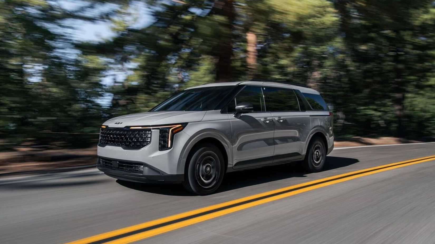 Plan dynamique 3/4 avant d'une Kia Carnival hybride 2026 roulant sur une route de campagne.