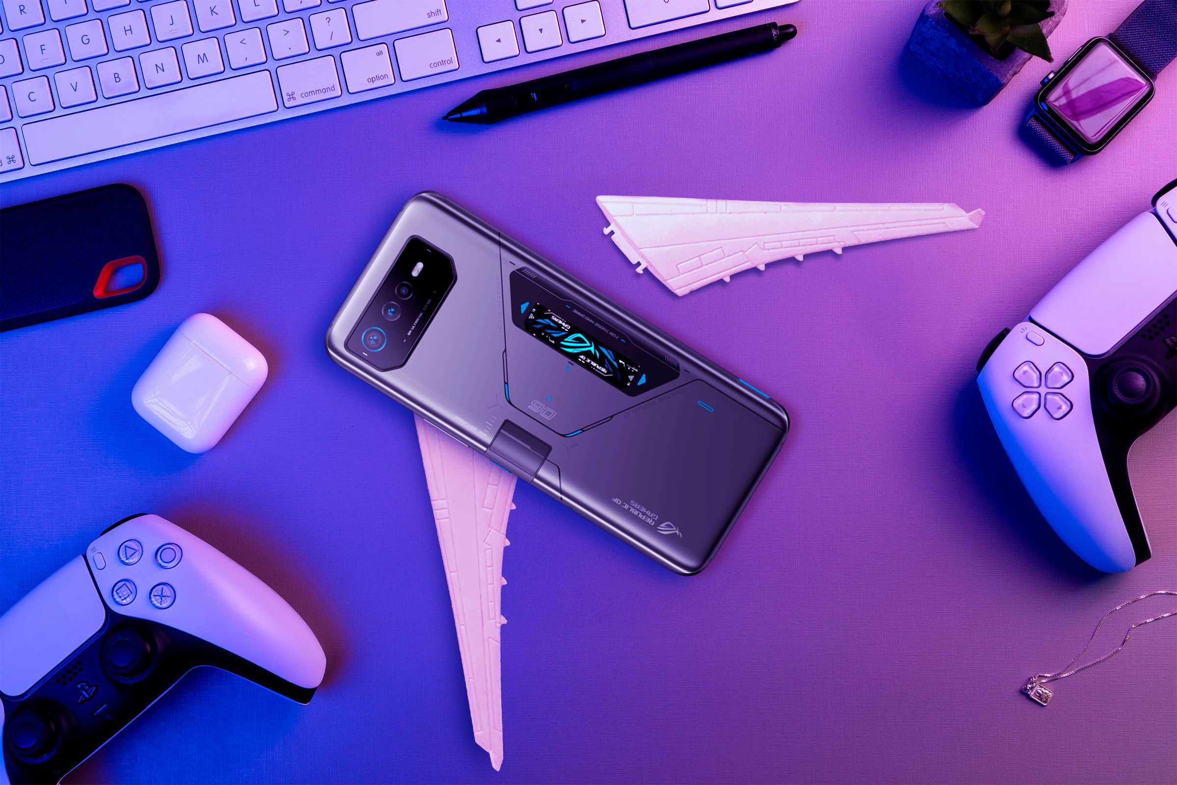 A gaming phone on a desk with broken wings and video game controllers beside it.