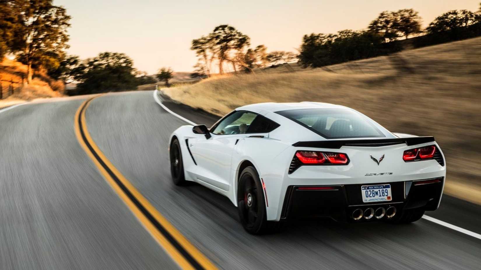 Dynamic rear 3/4 shot of a white 2014 Chevrolet Corvette C7 Stingray driving on a country road.