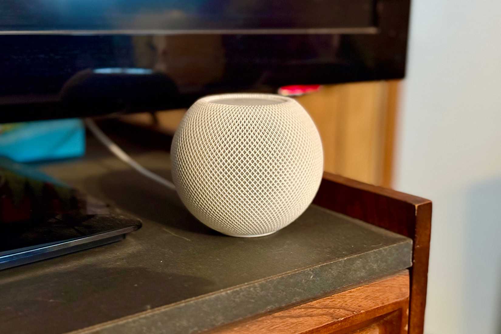 White HomePod mini in front of a TV.