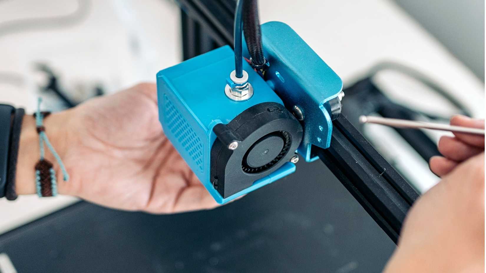 A person's hands are seen adjusting a 3D printer.