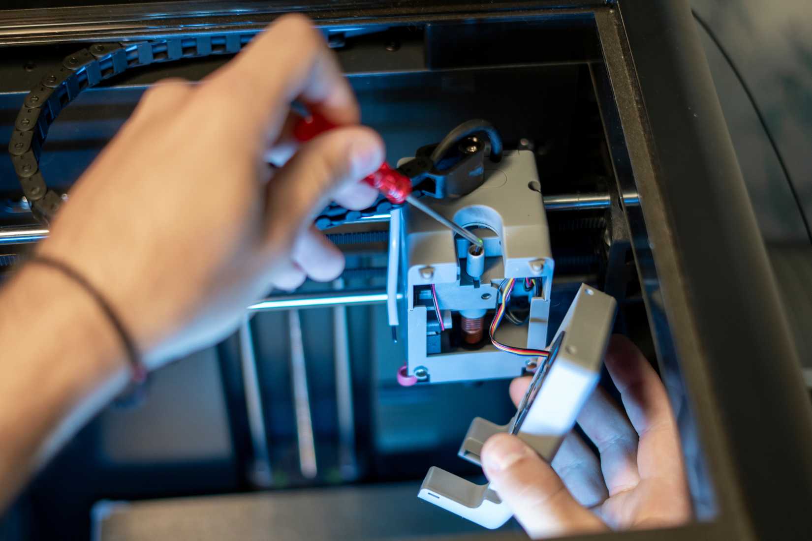 A person doing maintenance on the hot end of a 3D printer.