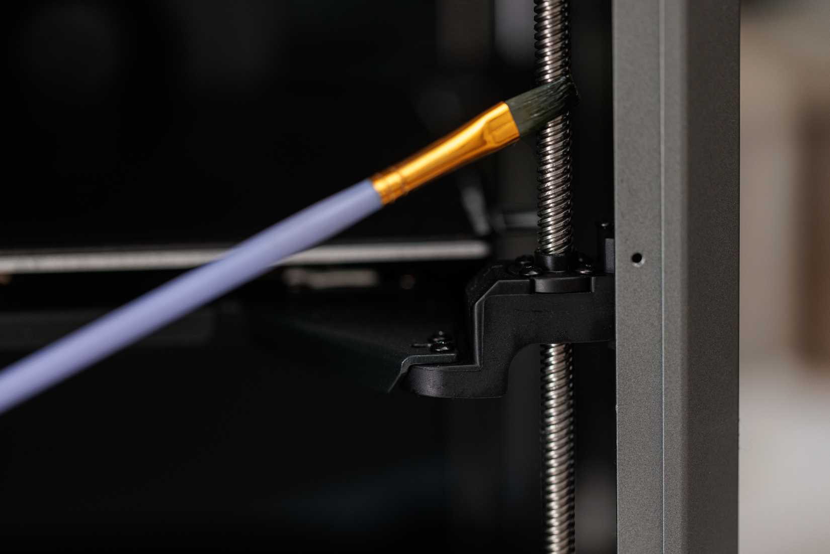 Applying lubricant with a brush on the threaded rod inside a 3D printer.