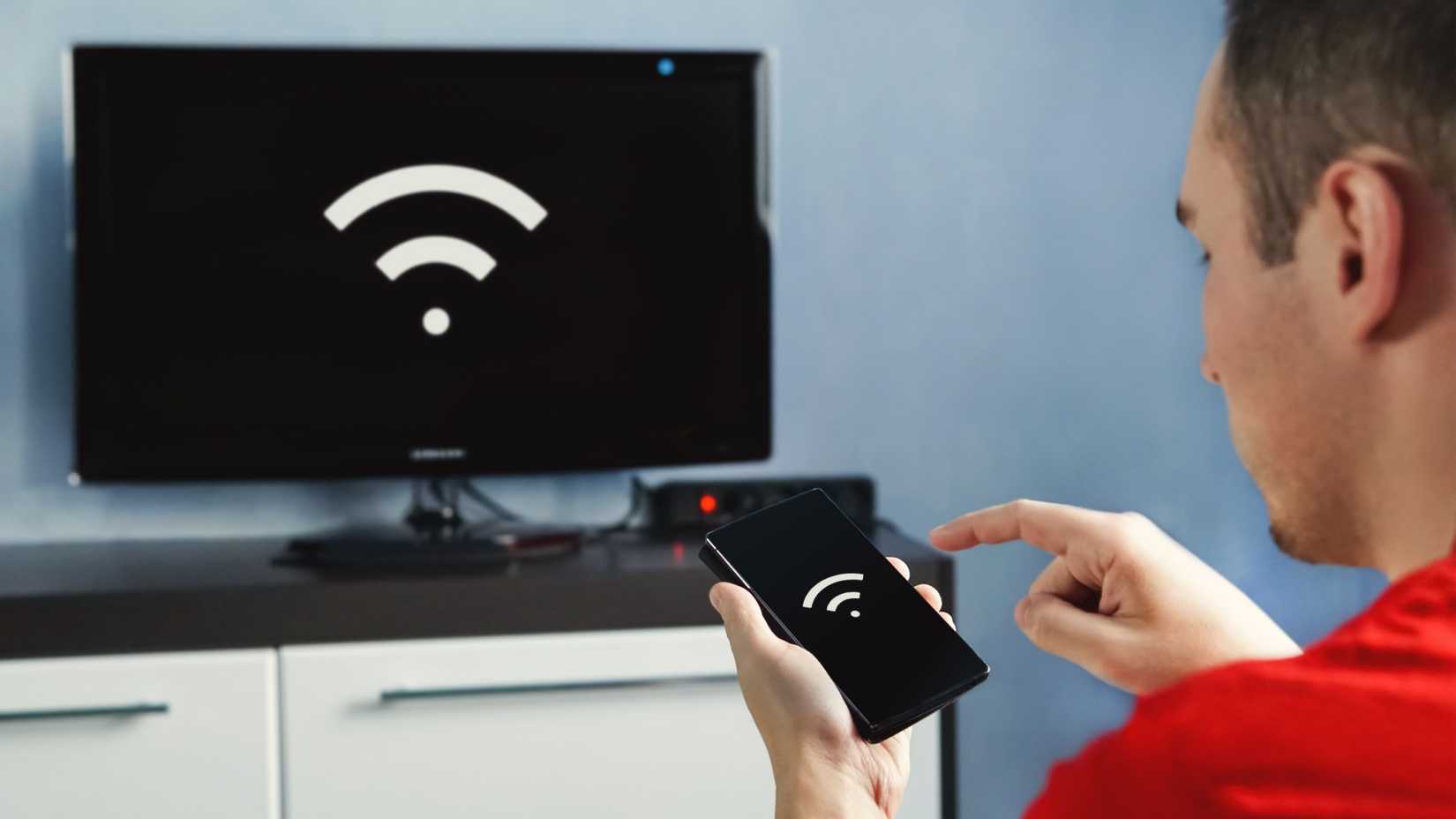 A man looks at the Wi-Fi sign on his phone echoed by the same sign on his TV.