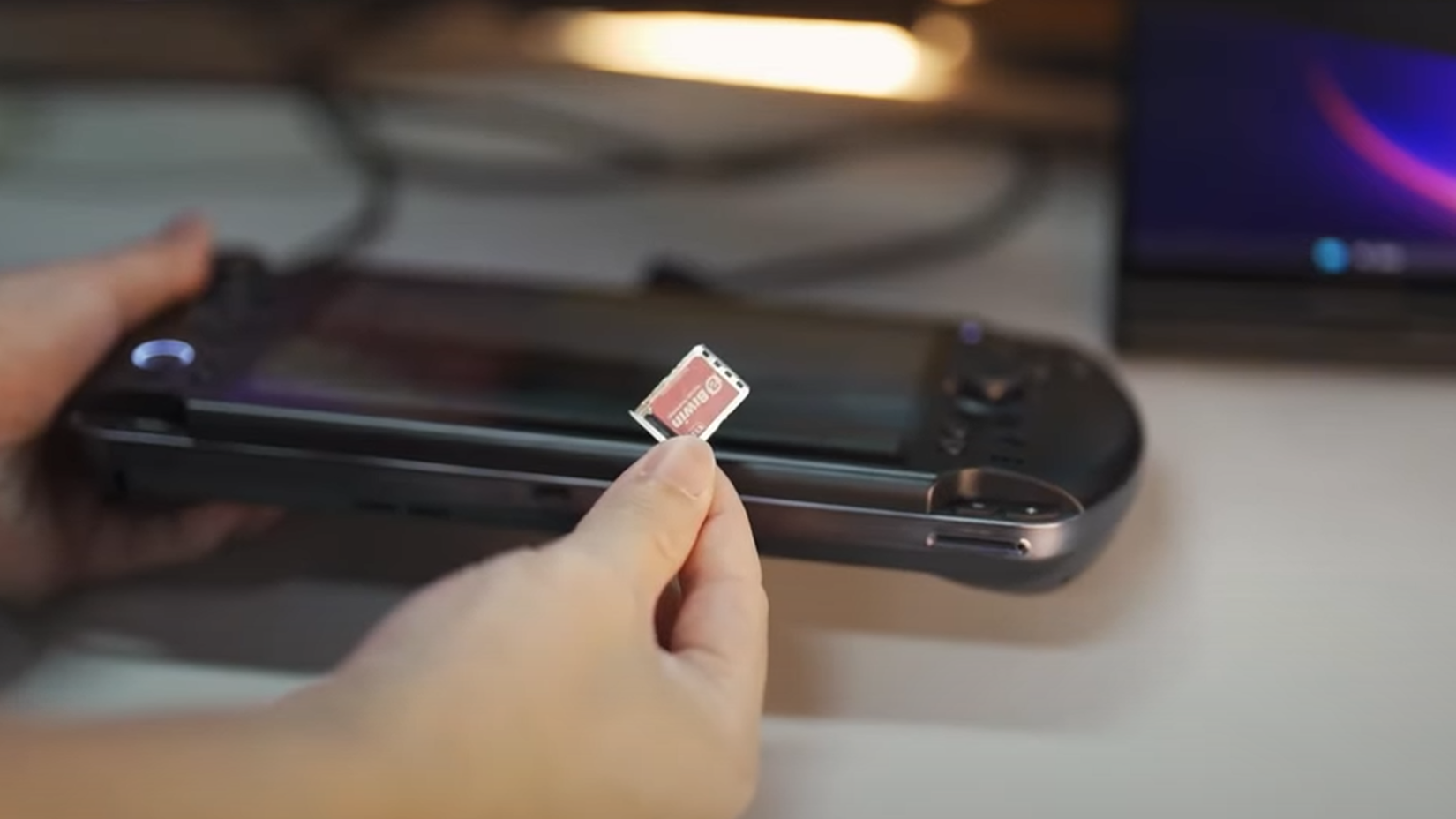 A person holding a Biwin Mini SSD, with a GPD Win 5 handheld PC in the background. 