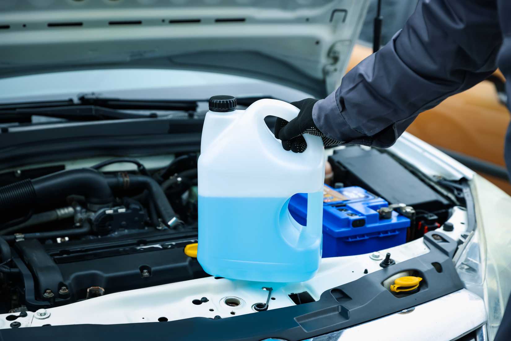 An image of a person holding extreme cold washer fluid over an engine about to fill the resevoir.