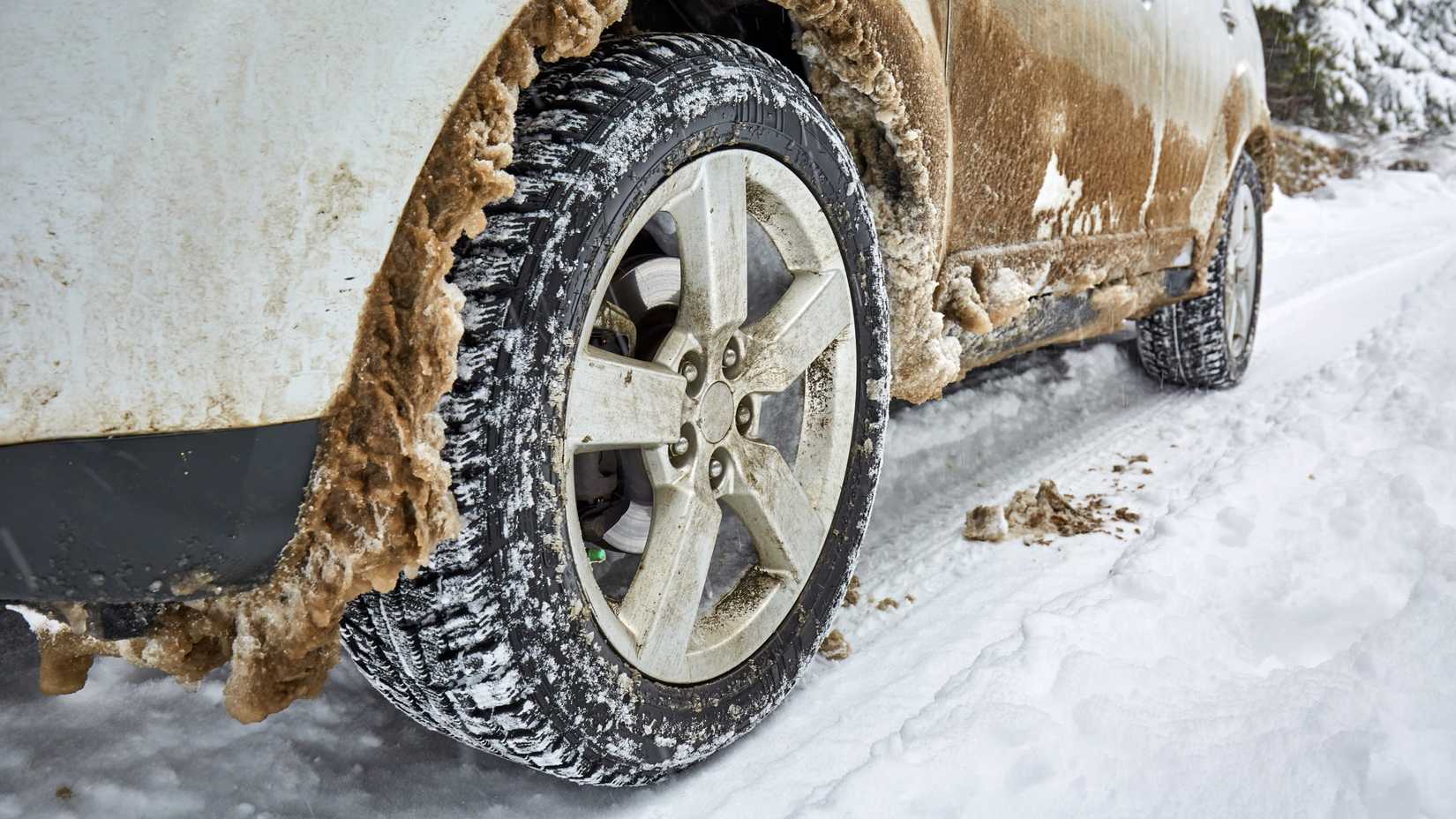 Late model white SUV with dirty and snow-covered tires.