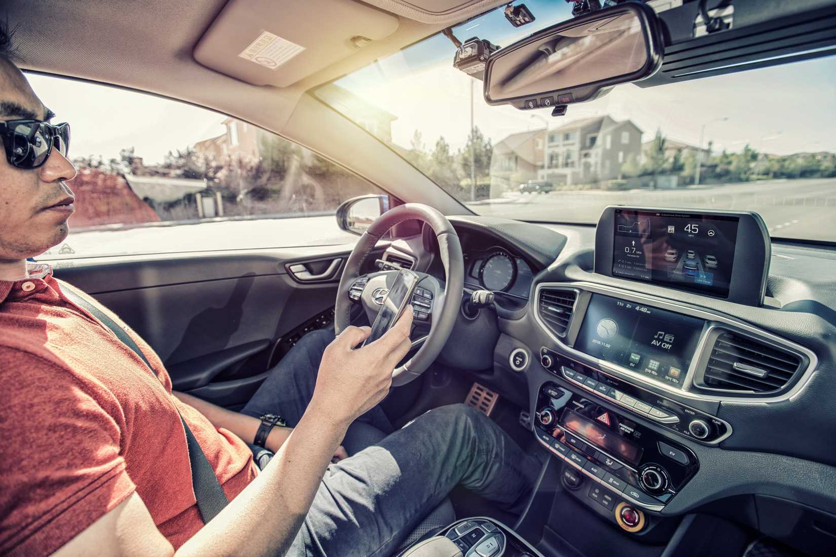 Man sitting in a Hyundai Autonomous Ioniq Concept, no hands on the wheel, holding his phone. 