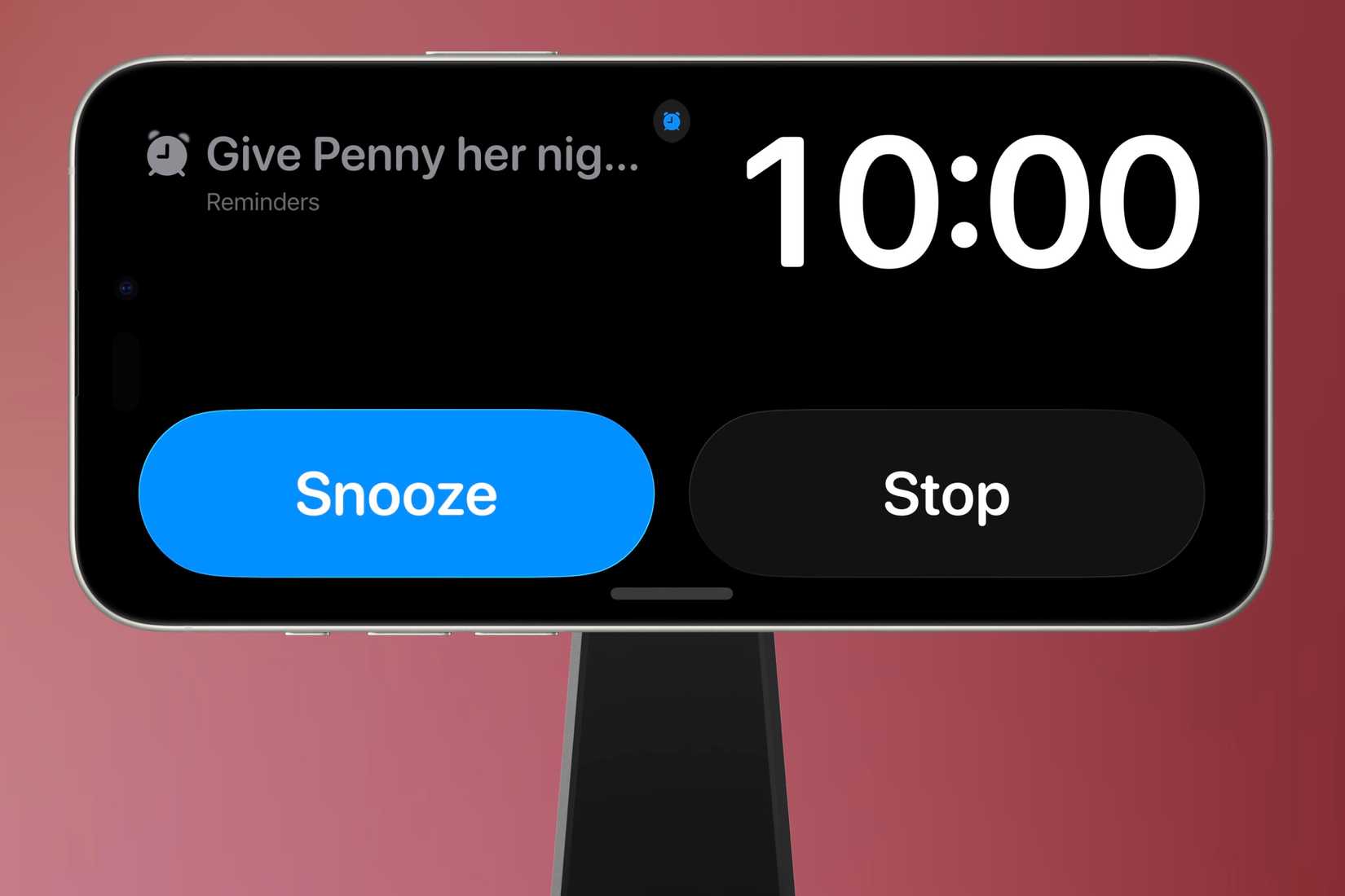 An urgent reminder alarm is going off while the iPhone is in Standby Mode on a MagSafe stand in front of a colorful background.
