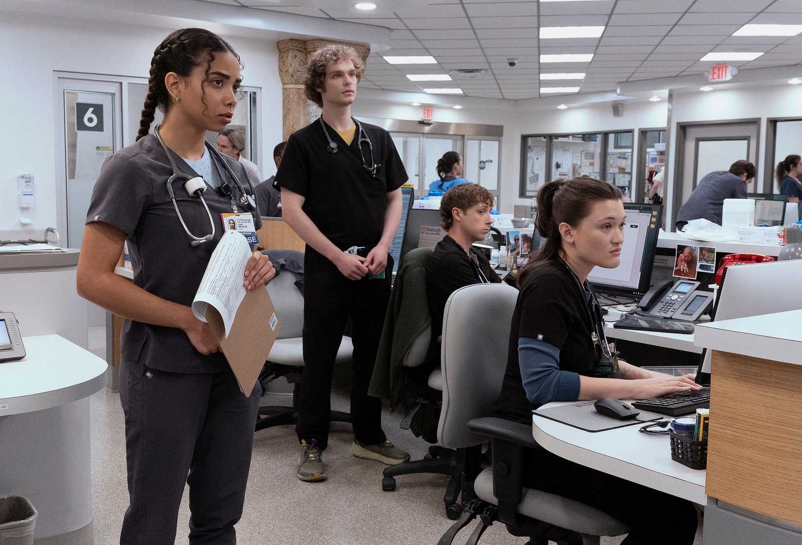 Laetitia Hollard, Lucas Iverson, Isa Briones y Gerran Howell como pasantes vestidos con batas, de pie y sentados en sus puestos.