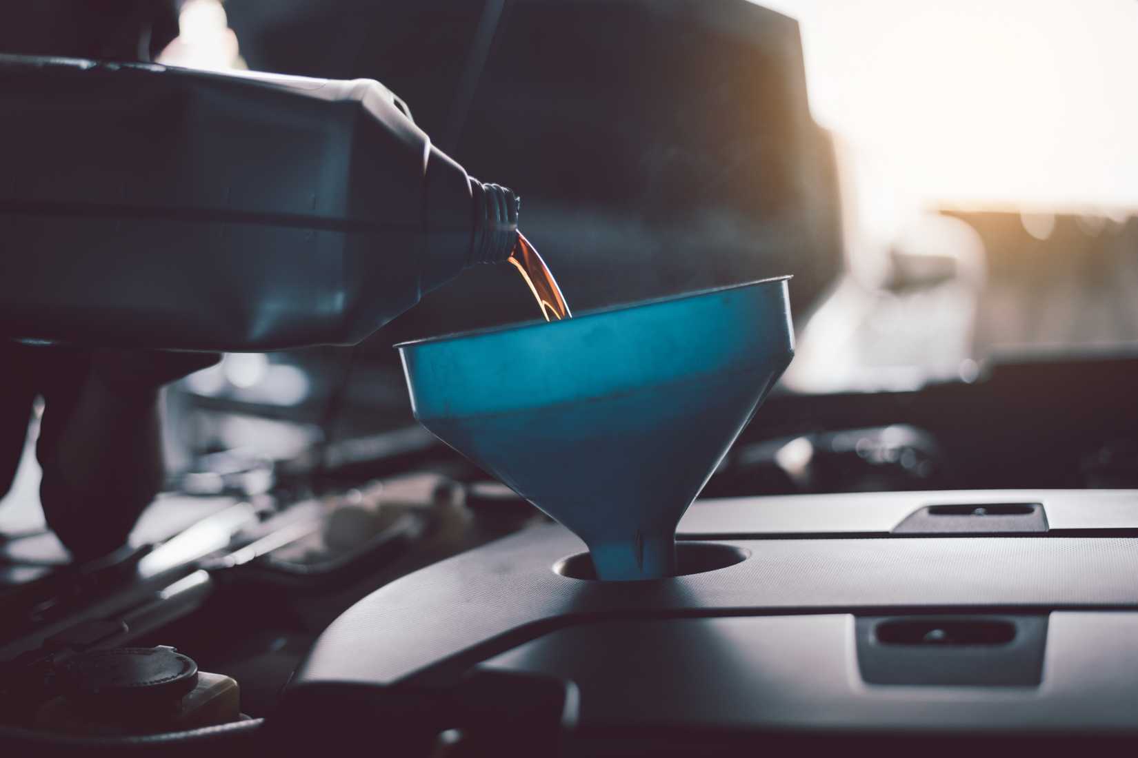 একজন মেকানিক একটি পুরানো মডেলের গাড়ির হুডের নিচে তেল পরিবর্তন করছেন।