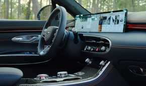 Close-up shot of the steering wheel and infotainment screen inside the cabin of a 2026 Genesis GV70.