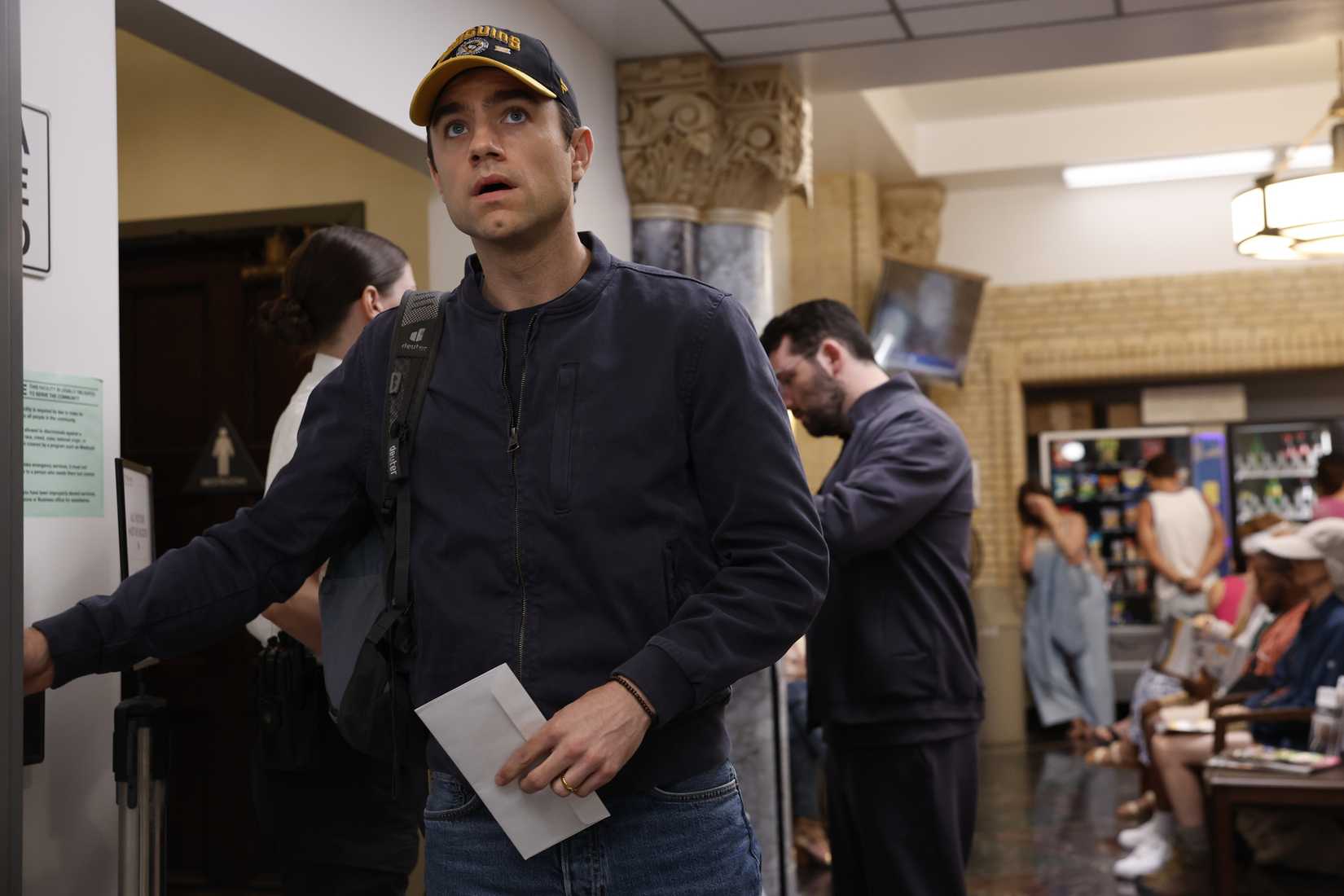 Patrick Ball como el Dr. Langdon con sombrero, chaqueta y mochila mientras regresa al trabajo.