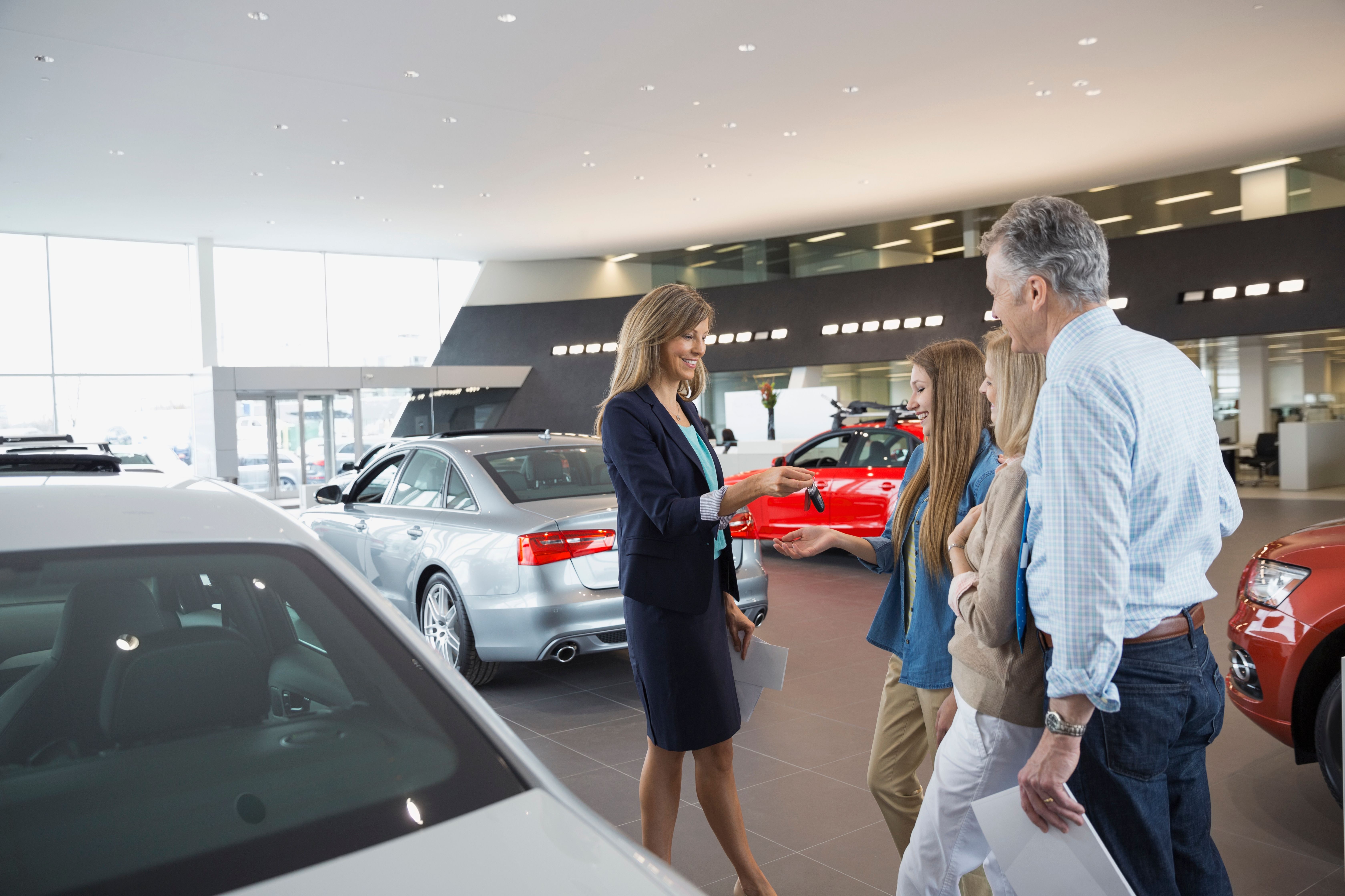 Salesperson in a dealership showroom handing a family keys to a new car.