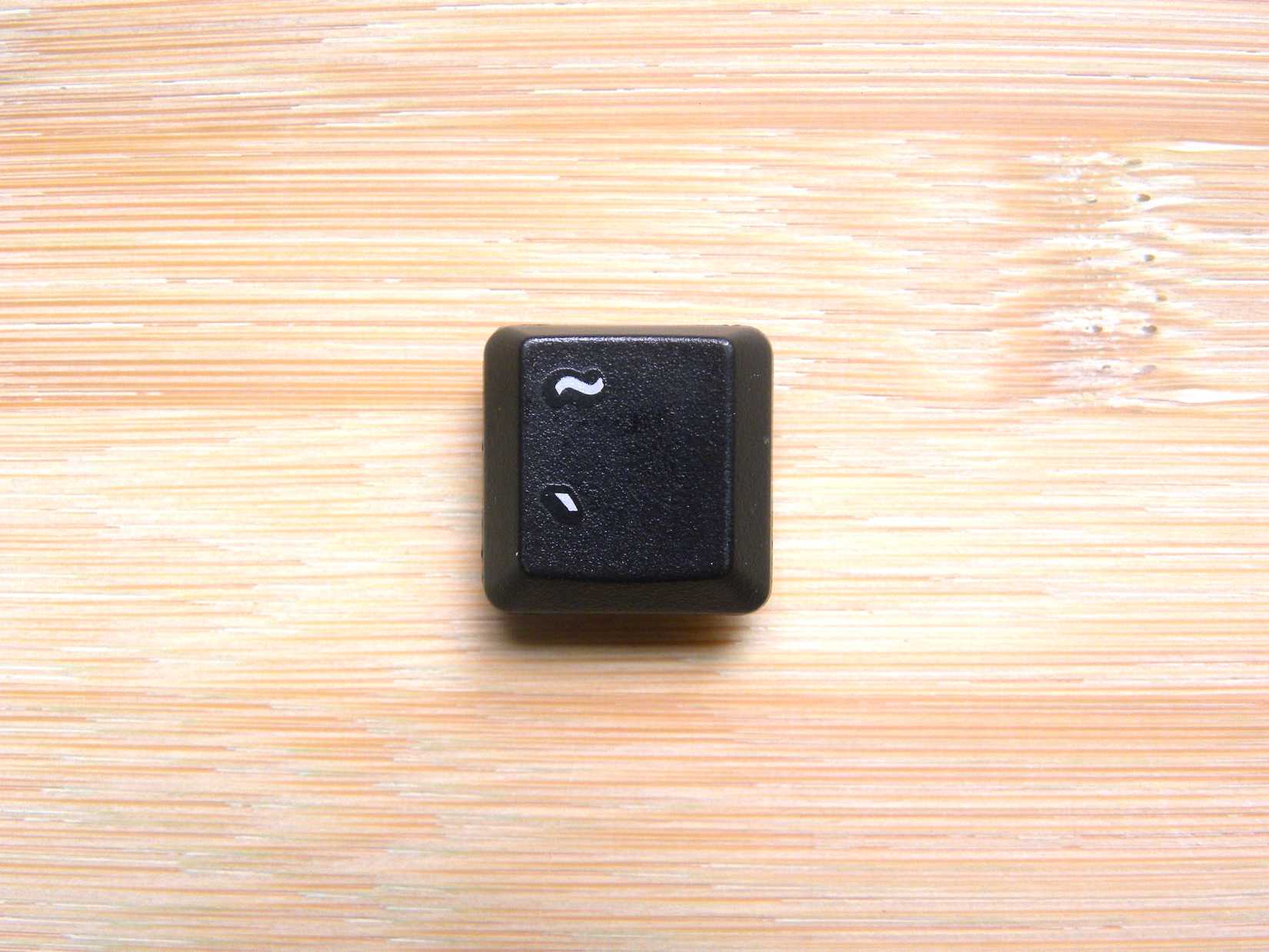 A keybaord tilde key on a woodgrain backdrop