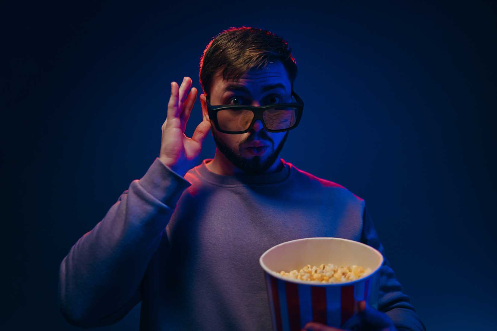 A man watching a movie cups his ears and seems pleased.