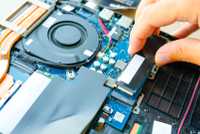 A hand inserts an SSD into a laptop.