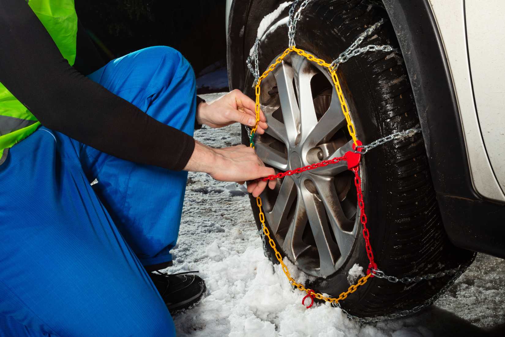 An image of a person inspecting snow chains on their tire.
