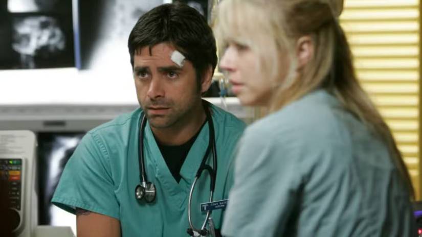 John Stamos in green scrubs with a stethoscope around his neck in ER.