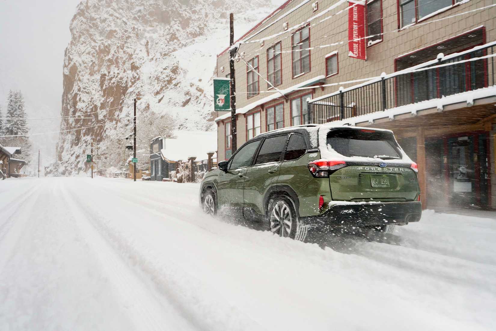 Green 2026 Subaru Forester Hybrid driving through snow in a downtown area.