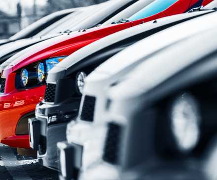 Front end of a single red car paked by other white and black cars