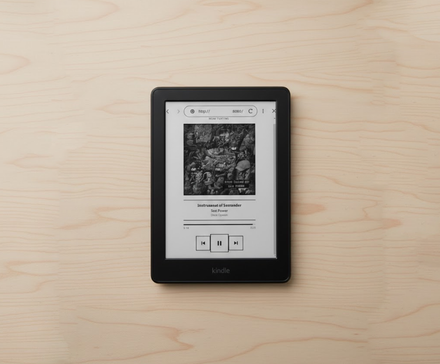 Kindle на деревянной поверхности, отображает панель со Spotify _Сейчас играет_.