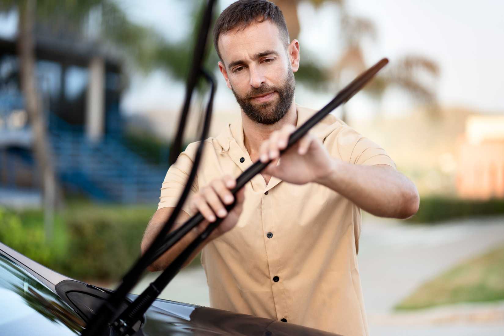 লোকটি তার গাড়িতে ওয়াইপার ব্লেড পরিবর্তন করছে।