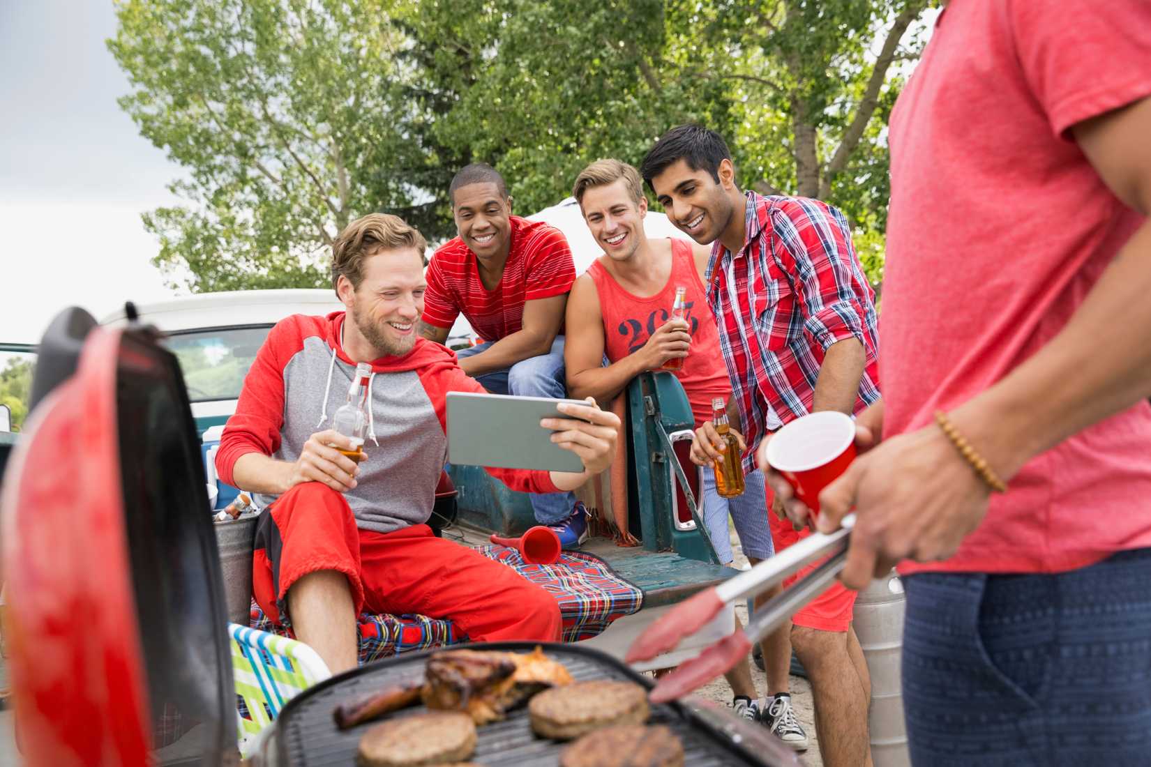 man tailgating with a group of friends in the back of a truck while grilling