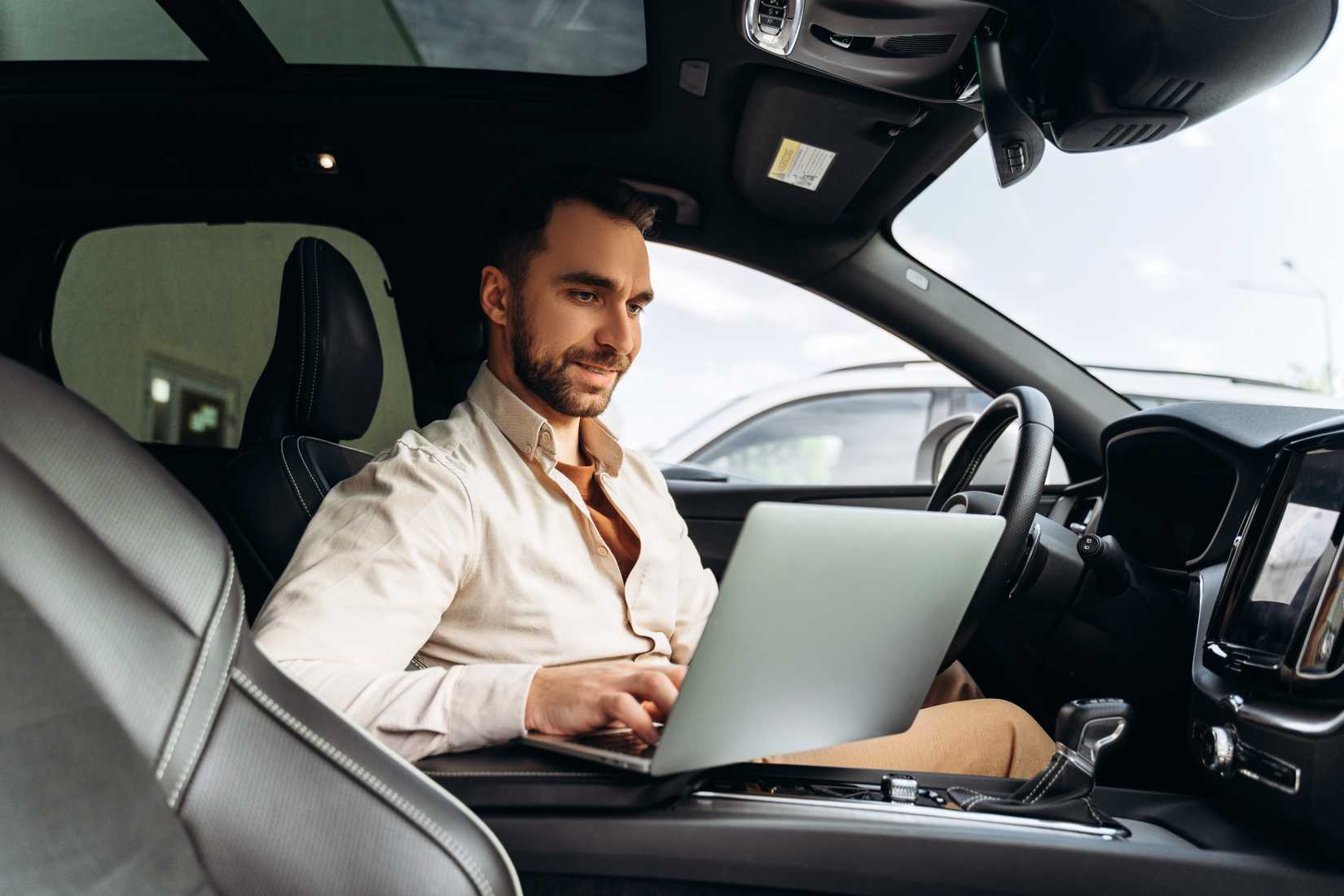 Photo of a man working on his laptop in the front seat of a late-model vehicle.