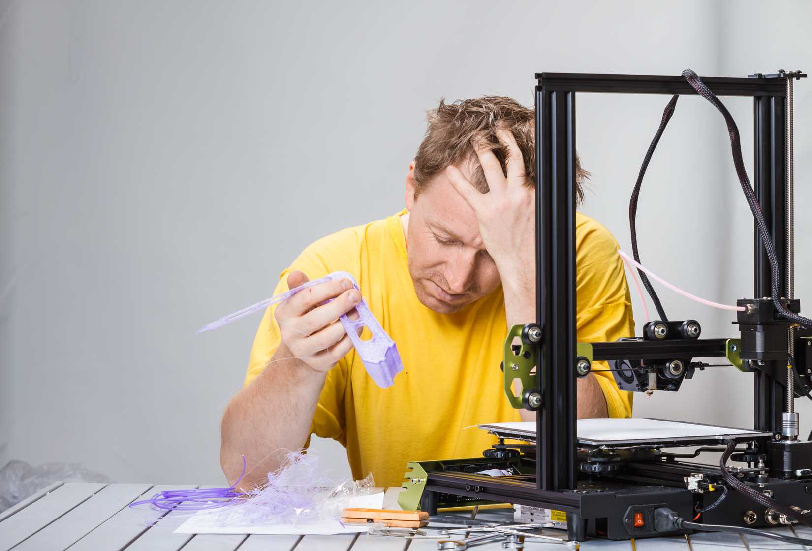 Un hombre luchando con una moderna impresora 3D con rizos de filamento.