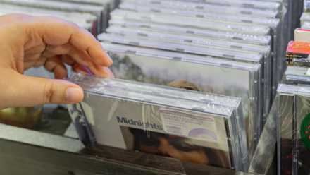 A hand selecting the “Midnights” album CD from a rack.