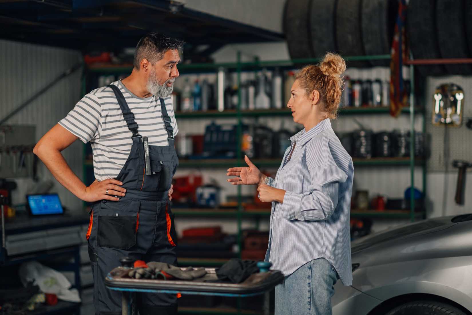 A woman speaking with a mechanic inside the shop about her car.