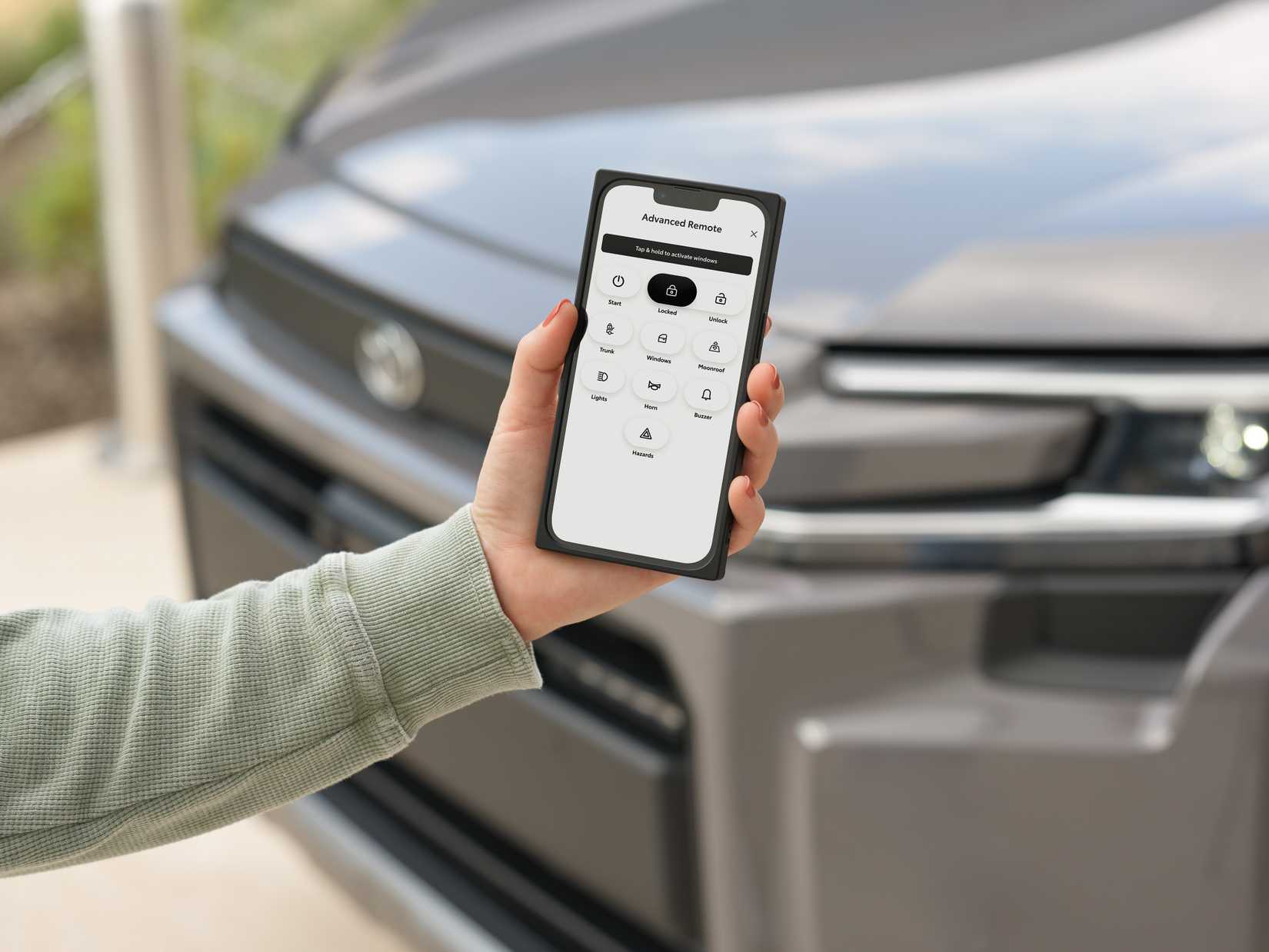 Toyota app shown on a smartphone being help up in front of a late-model Toyota vehicle.