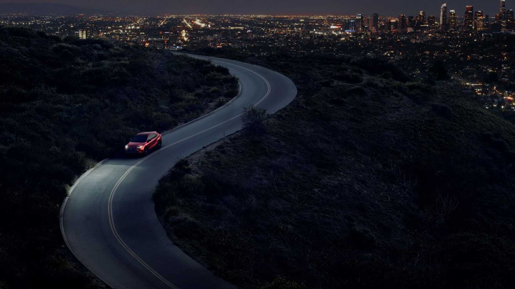Dynamic overhead front 3/4 shot of a red 2024 Toyota Venza Nightshade driving on a winding road.