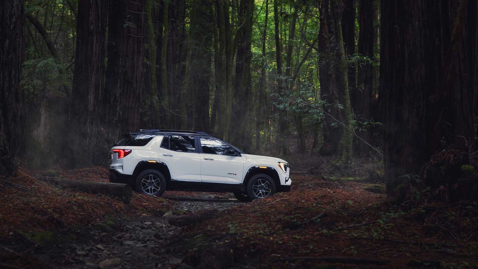 Side profile view of 2026 GMC Terrain AT4 in Summit White with two-tone roof crossing the forest.