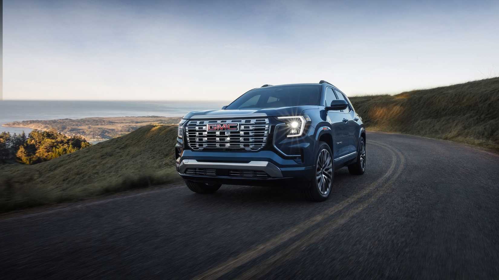 Front 3/4 view of the 2026 GMC Terrain in Raincoat Metallic driving on a winding road.