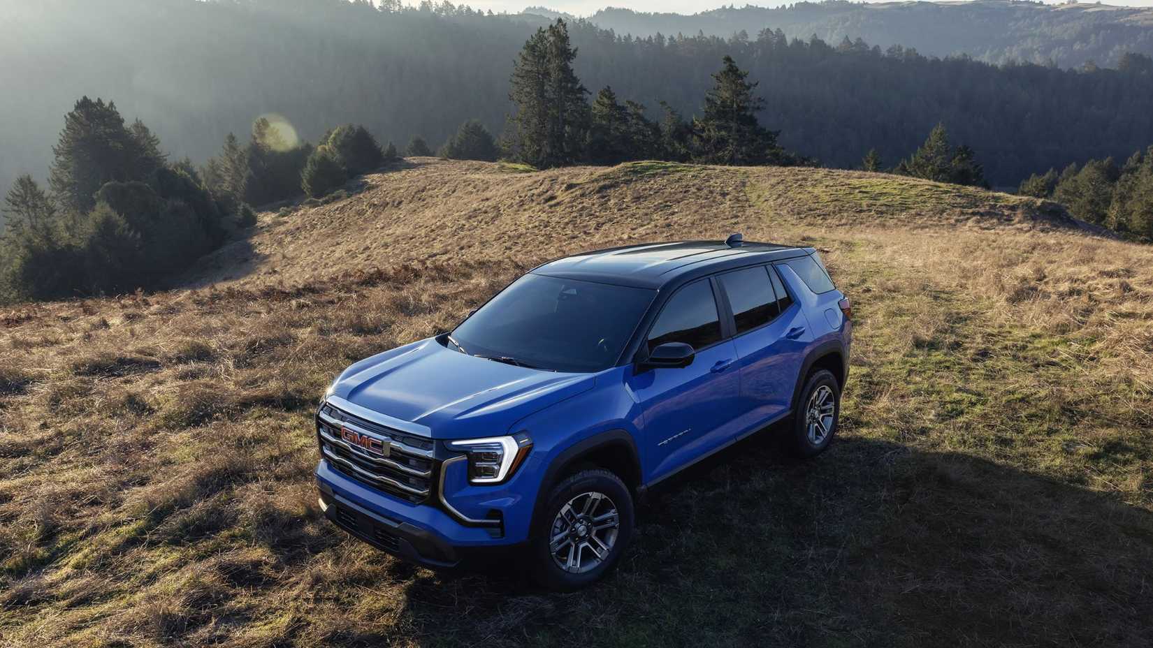 Front 3/4 aerial view of 2026 GMC Terrain Elevation in Rapids Metallic with two-tone roof parked in a field.