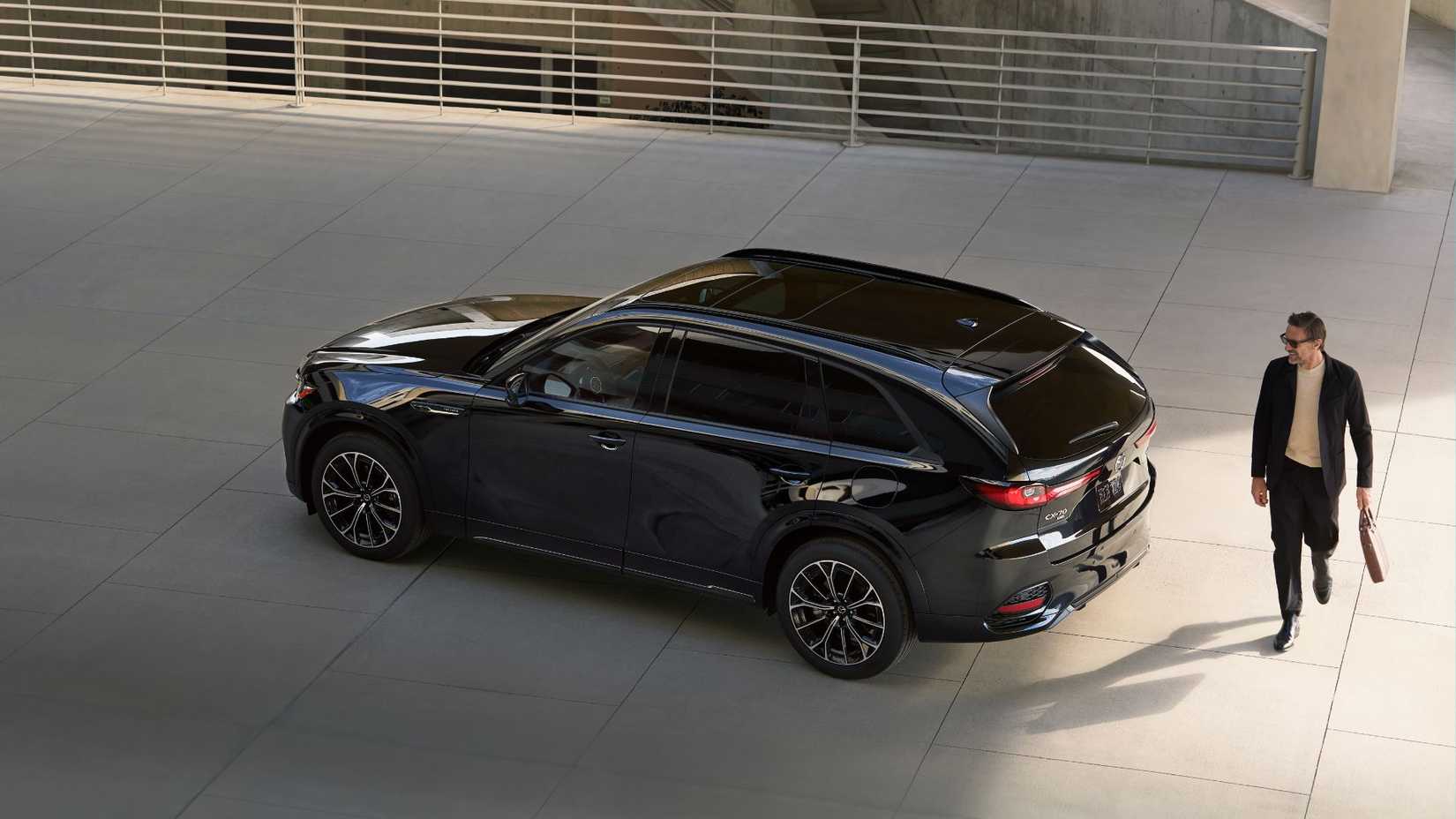 Static overhead rear 3/4 shot of a black 2026 Mazda CX-70 with a man walking behind.