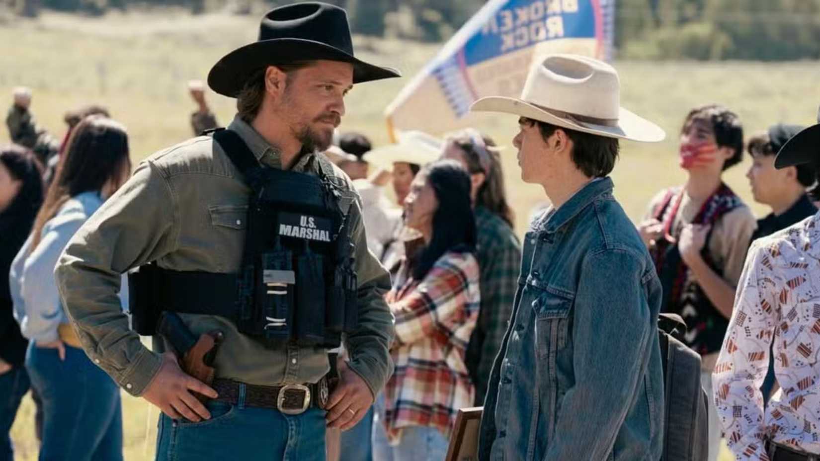 Luke Grimes as Kayce Dutton in U.S. Marshal vest talking to his son, Tate, in Marshals.